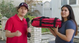 a man with a microphone and a woman holding a pizza in a warming box