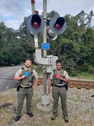 law enforcement officers holding safety cards near a railroad crossing signal