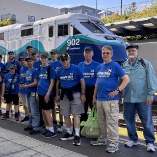 Rail campers wear ENS sign t-shirts in front of Sounder train.